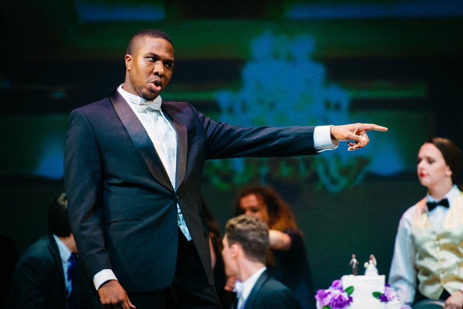 Gabriel Walker as Masetto in Don Giovanni, in black tie, pointing across the wedding party.