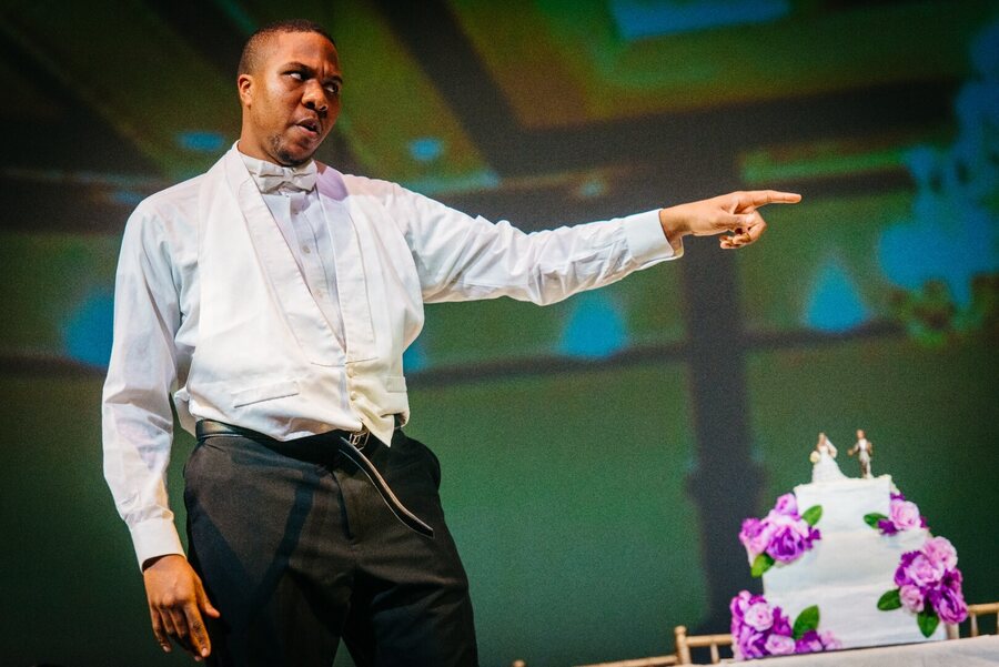 Masetto in shirtsleeves and waistcoat, pointing, the wedding cake behind him.